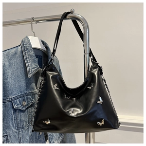 Detail of black leather tote bag with silver butterfly metal charms on denim jacket