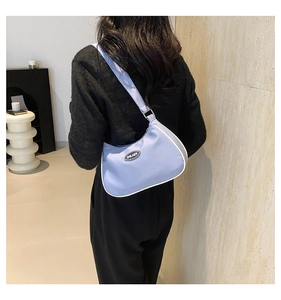 Detail of light blue nylon crescent bag with white piping and branded logo patch