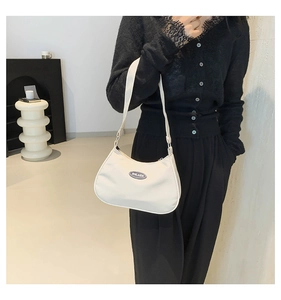 Close-up of cream nylon underarm bag featuring a minimalist circular logo on the front