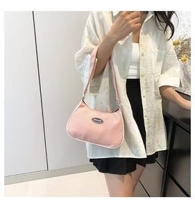 Close-up of pink nylon crescent bag with white piping and logo detail on model