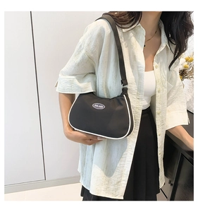 Detail of a black nylon crescent shoulder bag with white piping and logo by a model