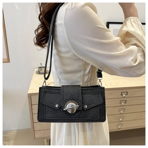 Detail of matte black crossbody bag with silver sphere buckle on model in home setting
