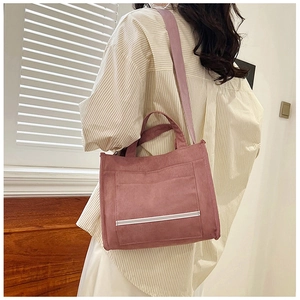 Detail of pink corduroy tote bag featuring striped front pocket and woven shoulder strap