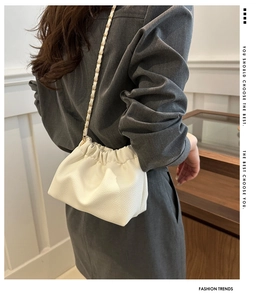 Detail of white drawstring bucket bag with gold chain strap on female shoulder
