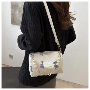 Detail view of cream-colored pillow bag with cartoon bear print and decorative pearl chain