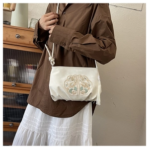 Detail van traditioneel bloemenborduurwerk en kwastje op een beige crossbodytas