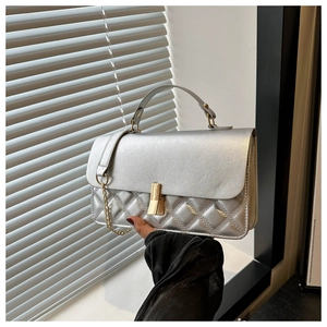 Detail einer silbernen Stepptasche mit goldenem Drehverschluss und Metallkettenriemen