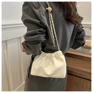 Close-up of cream faux leather bucket bag with gold chain and spherical metal bead detail