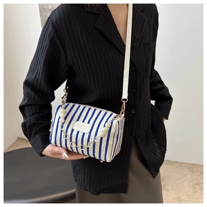 Detail of striped crossbody bag with elegant pearl chain and woven brand label