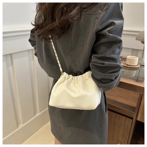 Side view of white pleated cloud bag with gold chain strap on shoulder in cafe setting