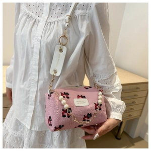 Detail of pink cylinder bag featuring black cat print, pearl chain, and wide strap