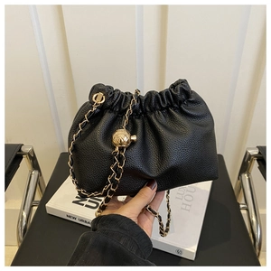 Detail of black pleated faux leather bucket bag with gold chain and metal ball ornament