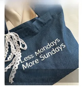 Détail du sac cabas en denim bleu avec nœud en dentelle blanche et texte artistique