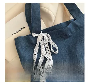Détail d'un sac cabas en denim bleu avec nœud en dentelle blanche et slogan imprimé