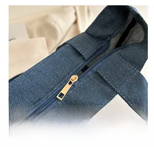 Gros plan d'une fermeture éclair dorée sur un grand sac cabas en denim bleu avec doublure