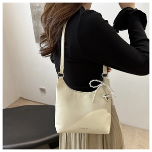 Détail du sac à bandoulière crème avec décoration de perles et pendentif cœur logo