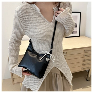 Détail du sac bandoulière en similicuir noir avec nœud en perles et breloque cœur