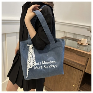 Détail du grand sac cabas en jean bleu avec texte et bordure en dentelle blanche