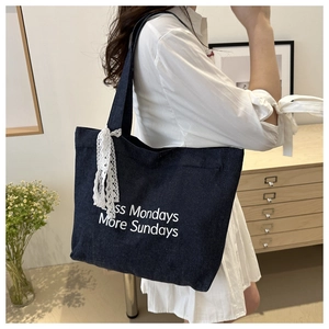 Détail du sac fourre-tout en denim bleu avec texte blanc et ruban en dentelle au manche