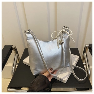 Détail du sac à bandoulière argenté avec nœud en perles, breloque cœur et gravure mode