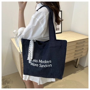Détail d'un grand sac cabas en denim bleu avec lettrage blanc et ruban en dentelle chic