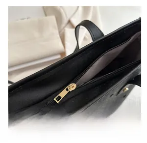 Close-up of smooth gold metal zipper and leather texture on a black tote bag