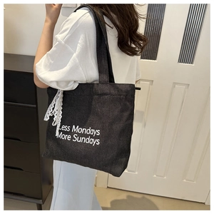 Détail du sac cabas en toile noire avec imprimé artistique et ruban en dentelle blanche