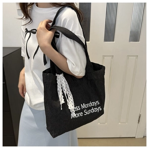Détail du sac fourre-tout en denim noir avec slogan et pendentif nœud en dentelle blanche