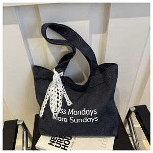 Détail du sac cabas en jean bleu avec slogan Less Mondays et nœud en dentelle blanche