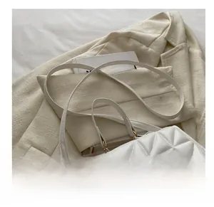 Close-up of white quilted handbag with golden metal buckle on a cream blazer