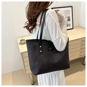 Detail of black tote bag featuring red heart patterns and CAIREE & HEXA brand label