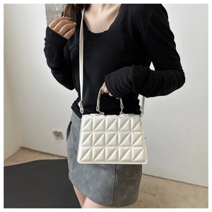 Detail of cream quilted handbag featuring a top handle and adjustable shoulder strap