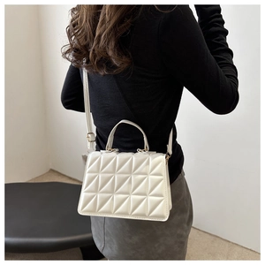 Detail of white geometric quilted handbag with gold hardware on a model outfit