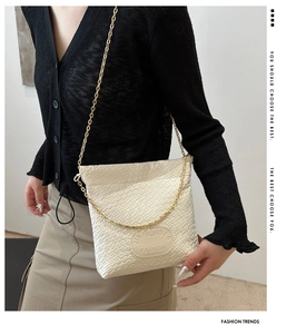 Detail of woven beige shoulder bag showing texture and gold chain strap on model