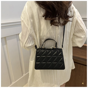 Detail of black quilted crossbody bag with top handle shown on a white blouse