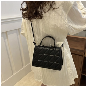 Detailed view of a black quilted crossbody bag with geometric triangle texture and gold strap