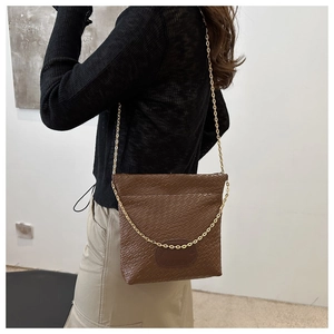 Detail of brown woven texture on bucket bag featuring golden chain strap and logo patch