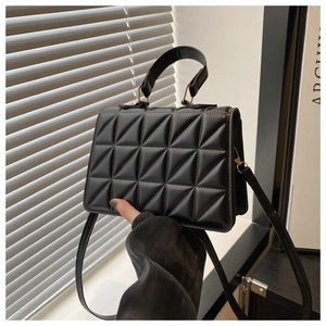 Detail of black quilted handbag featuring triangle embossed texture and gold hardware