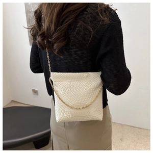 Detail of white woven texture crossbody bag with gold chain strap on female model