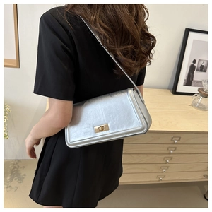 Silver metallic leather shoulder bag with gold twist lock shown on model in a modern home