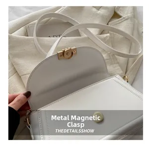 Detail of white square crossbody bag showing golden metal magnetic buckle and clean stitching