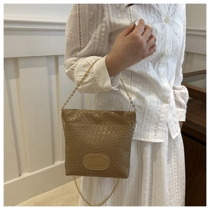 Detail of tan woven bucket bag featuring gold chain strap and circular logo patch