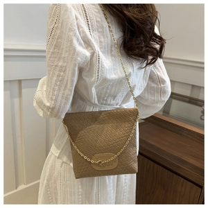 Detail of a brown woven leather crossbody bag featuring a gold metal chain strap on a model