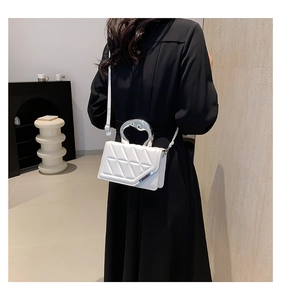 Detail of white quilted crossbody bag with unique silver metallic handle worn by a model