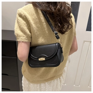 Detail of a minimalist black leather crossbody bag with a chic golden metal clasp