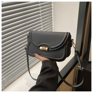 Detail of black leather flap bag featuring golden cylindrical metal buckle and stitching