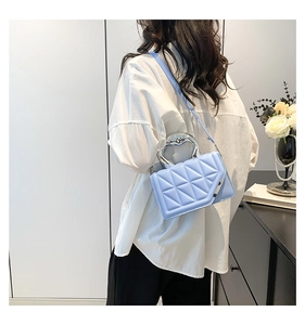 Detail of light blue quilted crossbody bag featuring unique silver heart-shaped metal handle