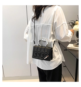Detail of black quilted crossbody bag with silver curved metal handle on model