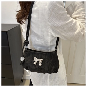 Detail of crossbody bag with silver metal bow and beaded strap on white shirt