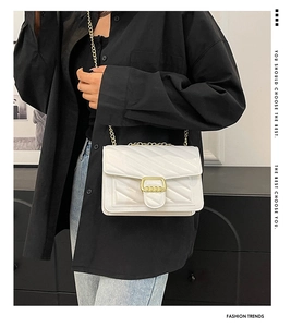 Detailed view of white quilted crossbody bag with gold chain strap on black shirt background